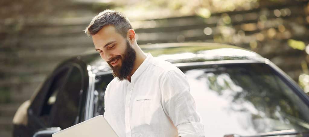 stylish businessman standing near the car and use the laptop 1